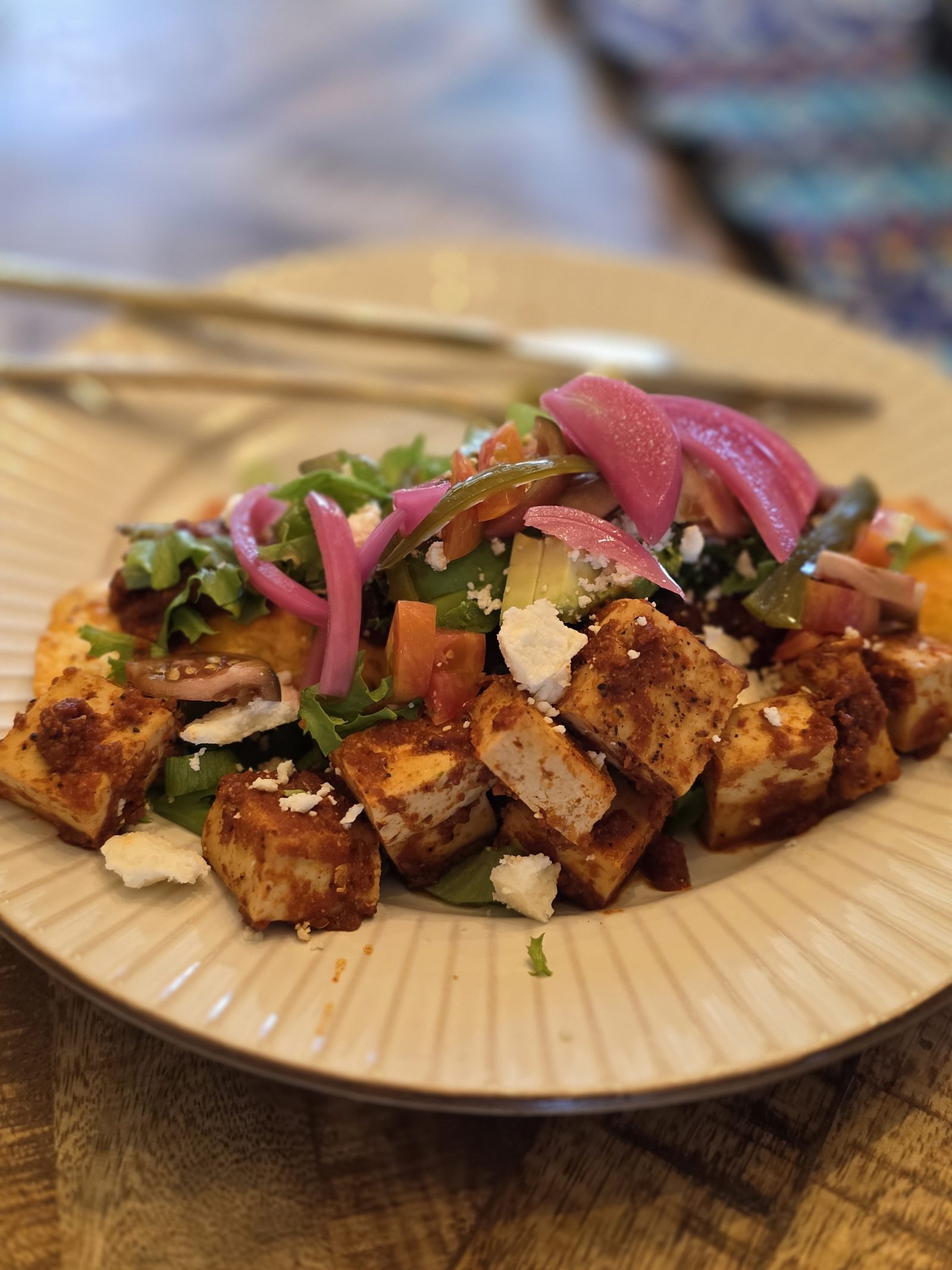 A vegan take on enchiladas Cuchicuato — tofu in a deep red chile sauce with crumbled cheese, pickled red onion, avocado, tomato and greens