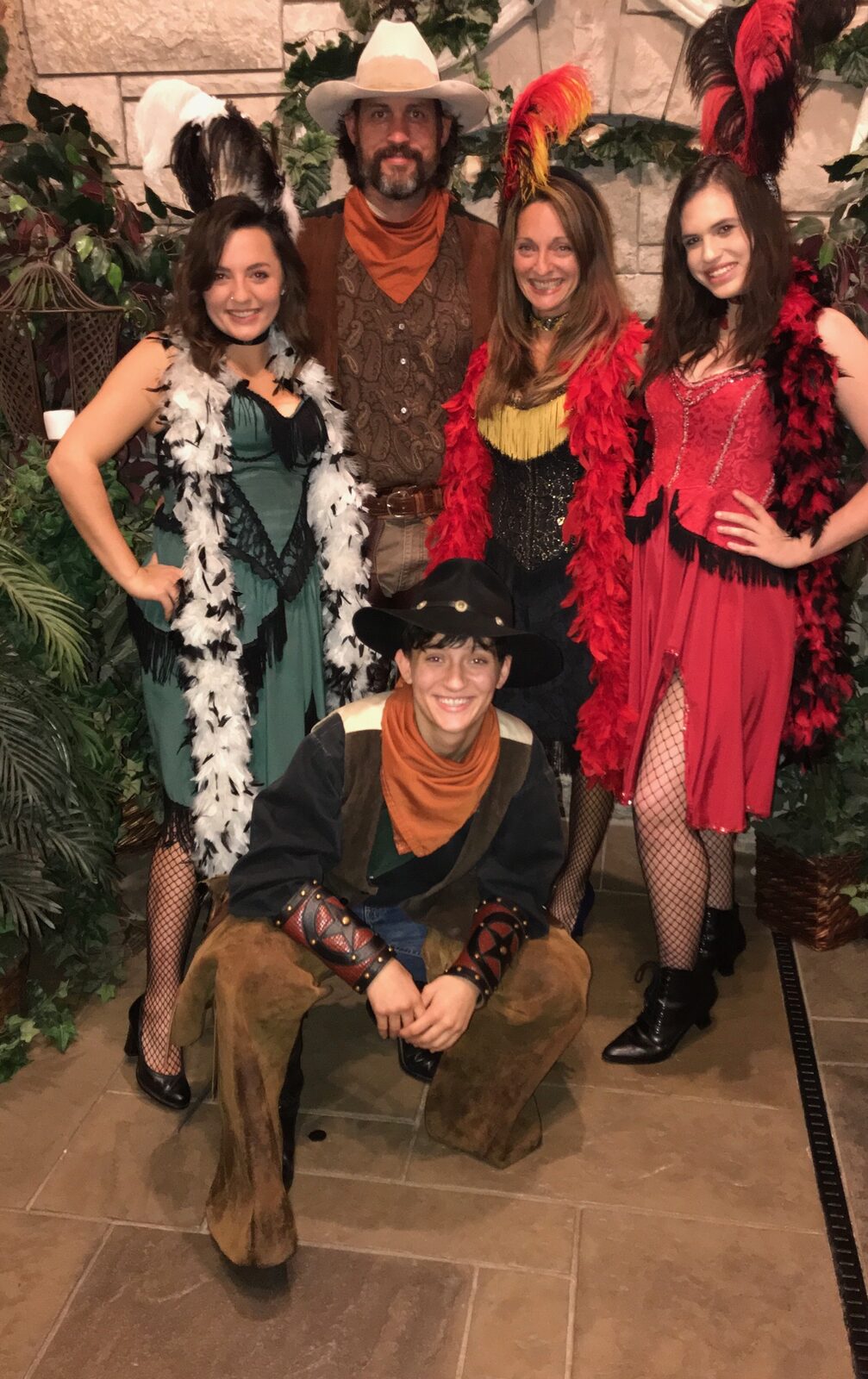 Old-west saloon-themed wedding photo with bride, groom, and bridal party in feather boas and cowboy hats