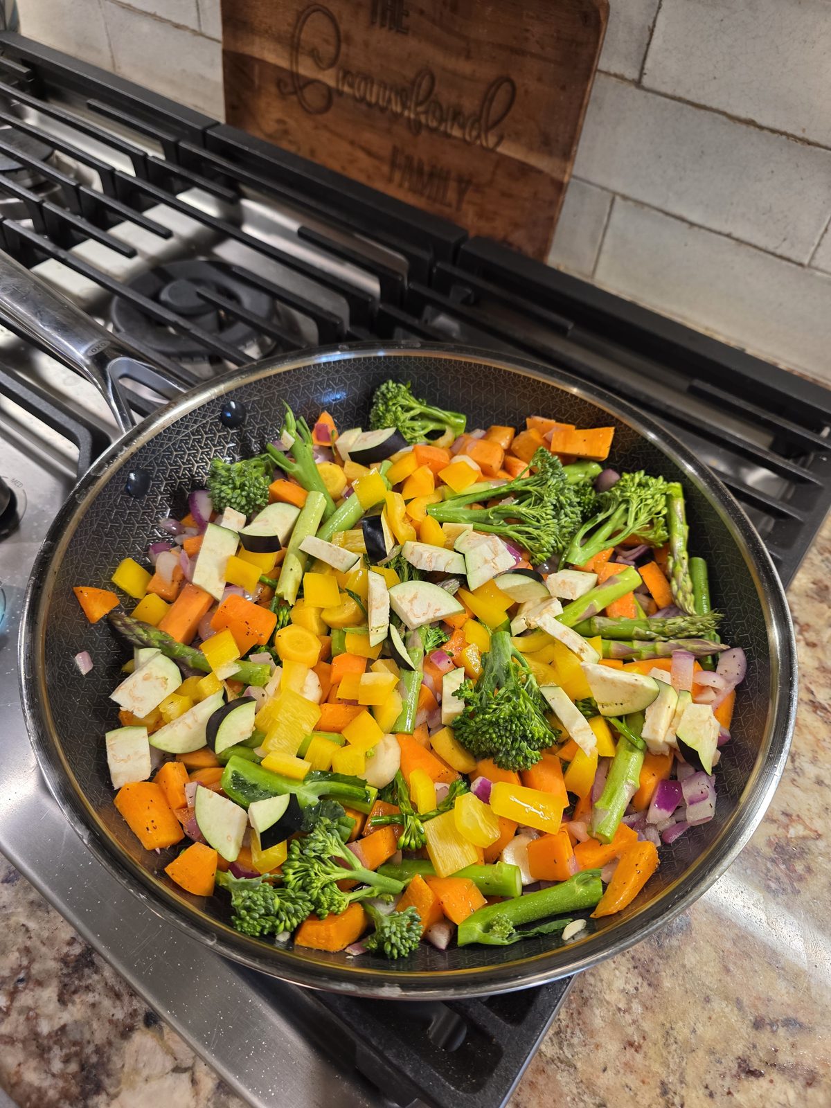 Skillet of chopped yellow bell pepper, garden eggplant, yellow carrots, red onion, broccolini and asparagus ready to sauté