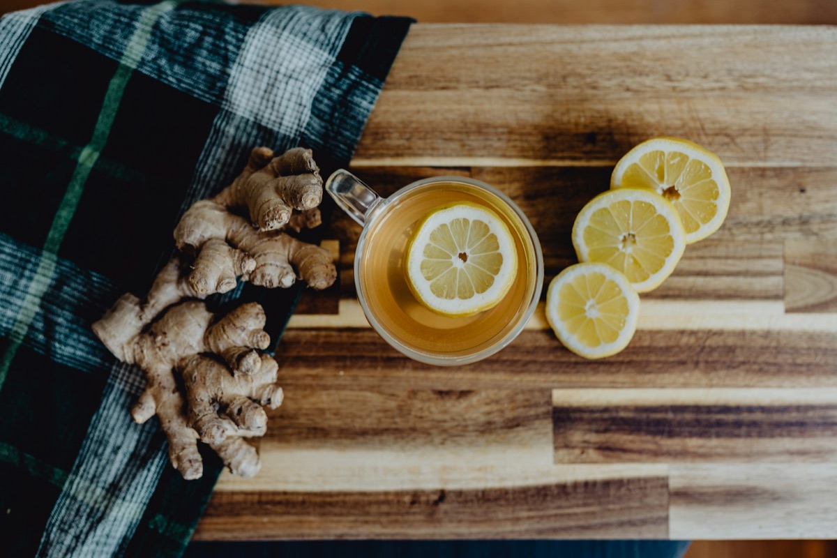 A cup of green tea with fresh lemon and ginger on a wooden table in warm light