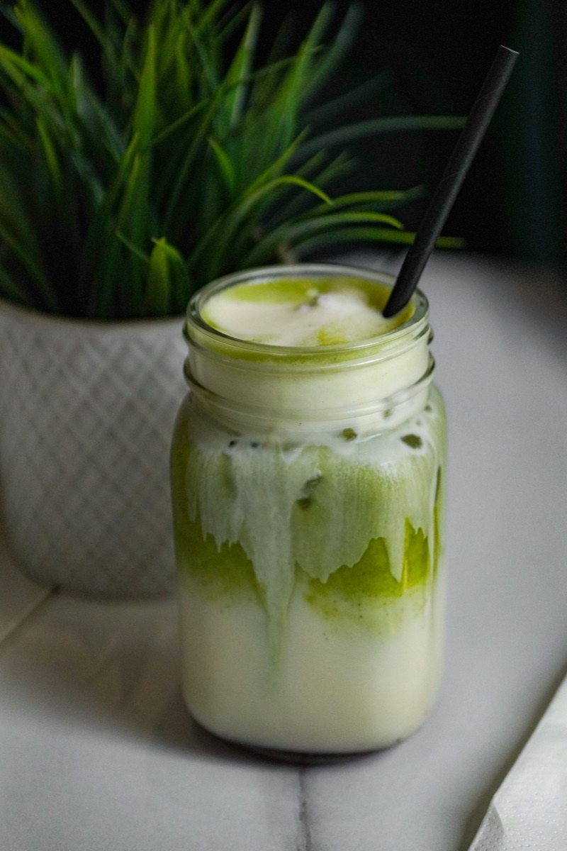 An iced green tea latte in a glass with a straw