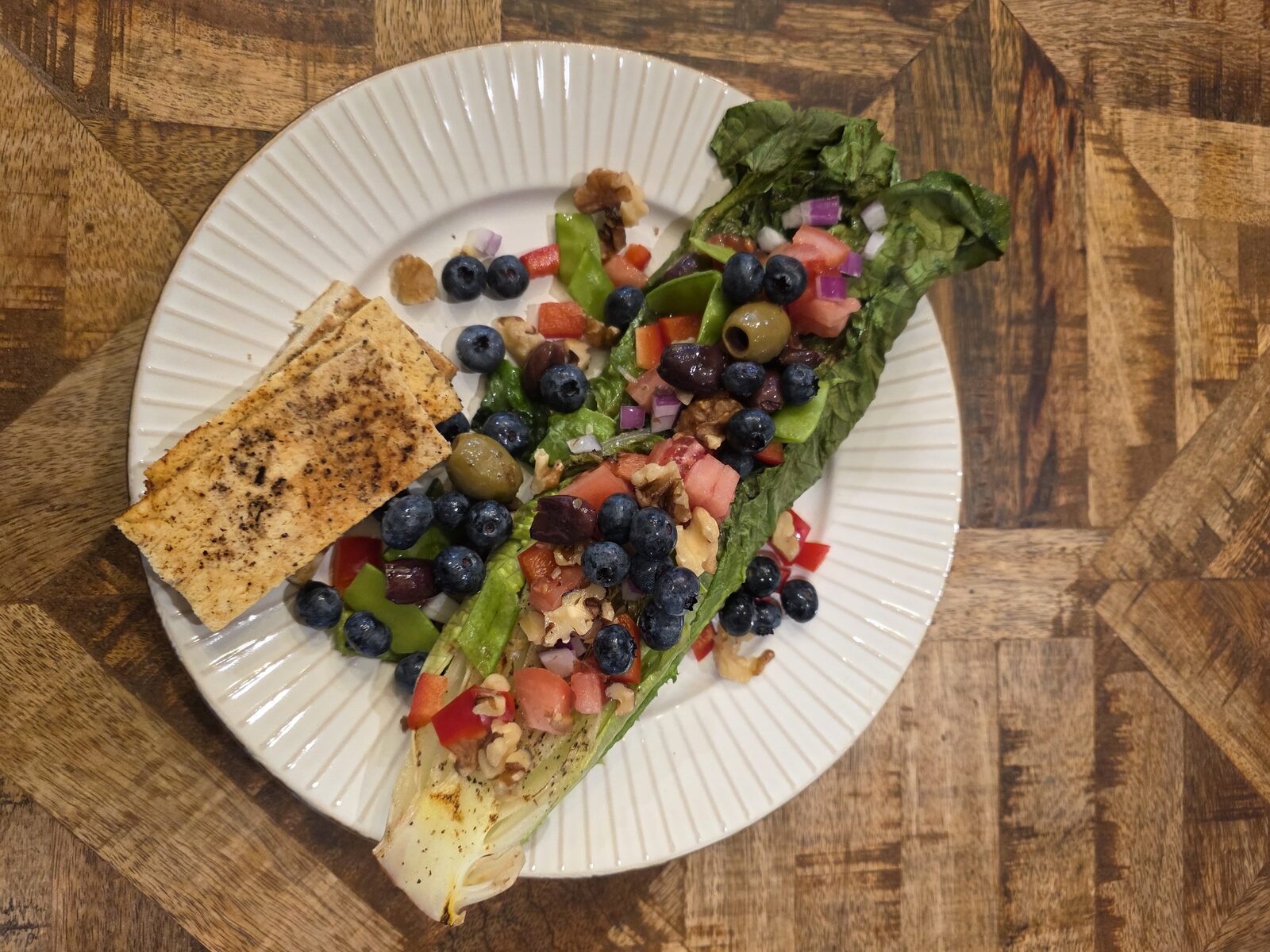 A grilled romaine salad topped with tomatoes, red pepper, olives, and walnuts — the carotenoid-rich colors this post is about