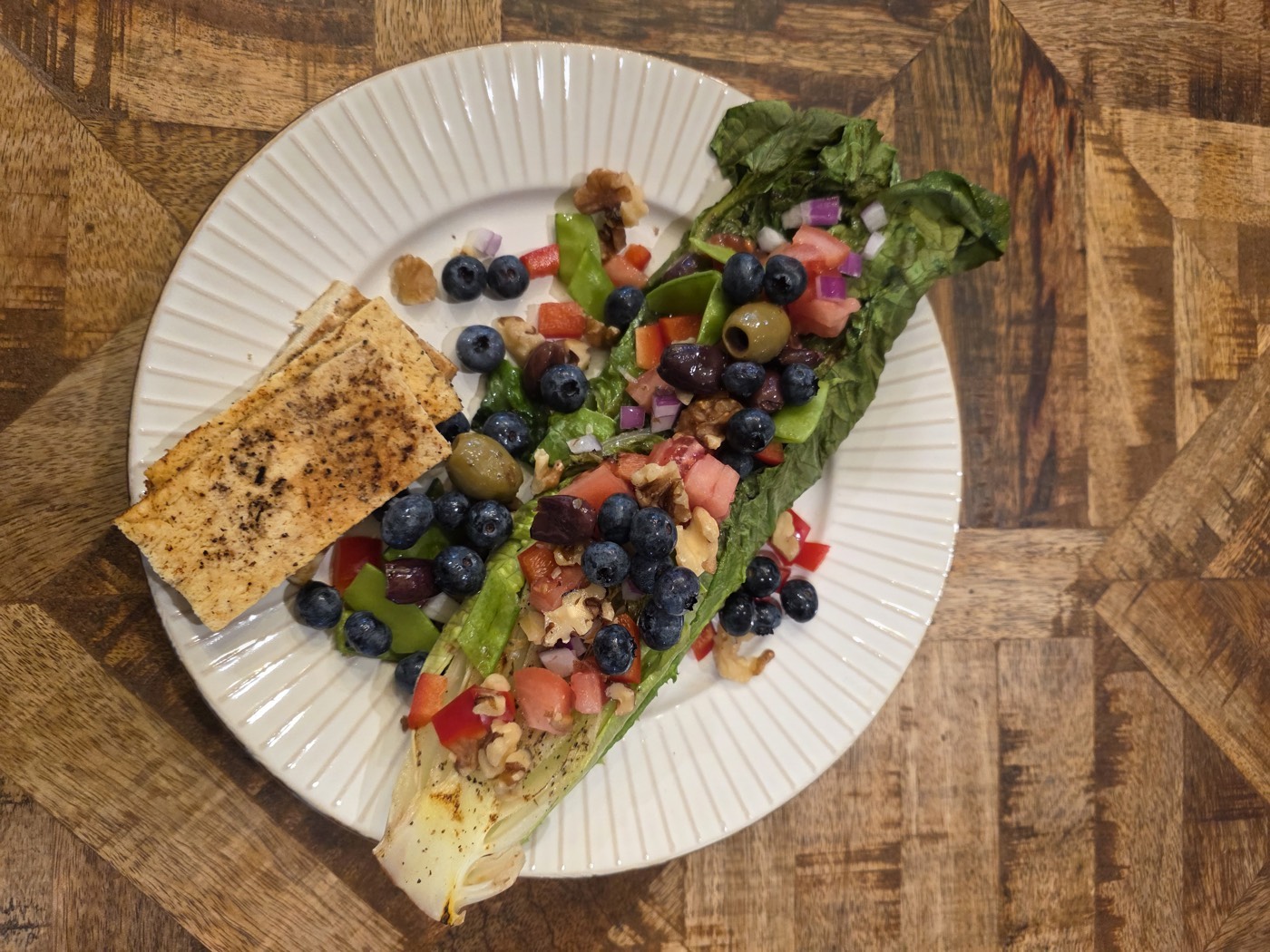 Grilled romaine heart topped with blueberries, tomato, olives and walnuts, with a piece of grilled flatbread