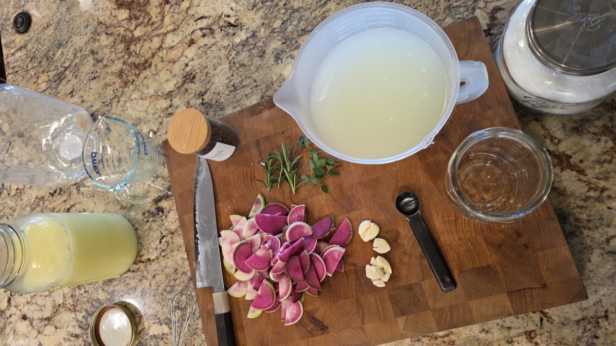 Sliced watermelon radishes with rosemary, oregano, and smashed garlic on a butcher block