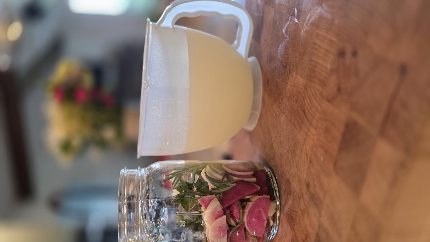 A jar packed with sliced watermelon radishes beside a jar of fresh golden whey, ready to begin fermentation